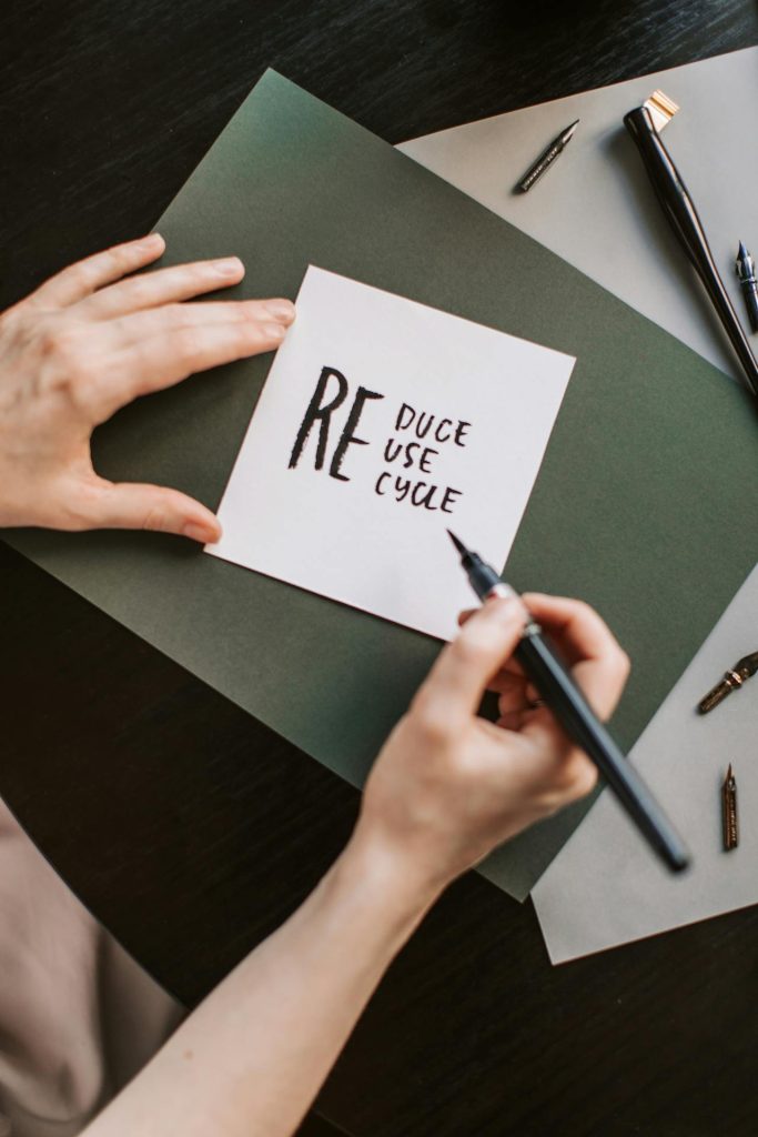 Hands writing “Reduce Reuse Recycle” on a card, symbolizing ESG packaging and waste reduction at M&Y Global Solution